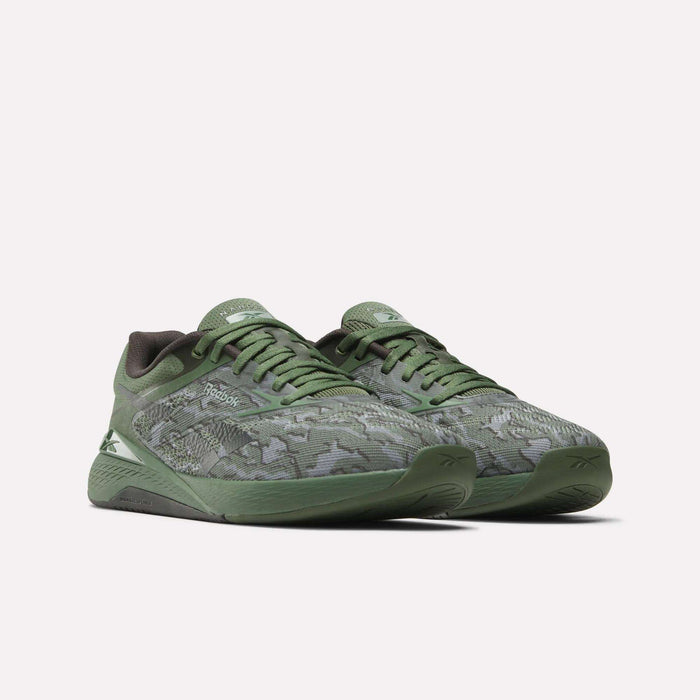 The Reebok Nano X5 Training Shoes for men feature a green camouflage pattern, dark green soles, and Reebok logos on the side and tongue. These iconic shoes are displayed against a plain white background.