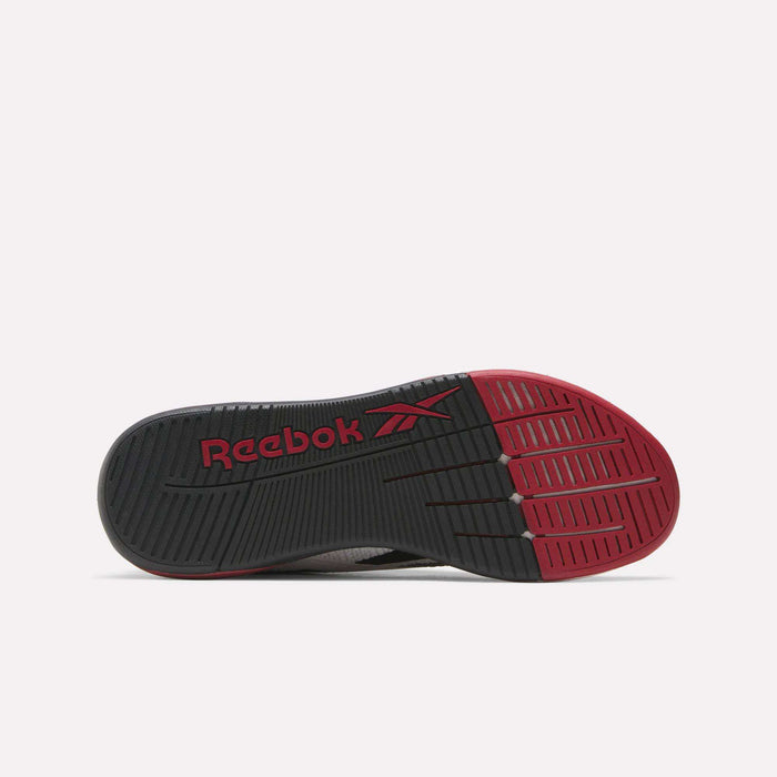 The image shows the sole of the Reebok Nano X5 Training Shoes for men, featuring a mostly black design with deep traction grooves, a striking red toe area, and a bold Reebok logo that add contrast and style to this versatile trainer.