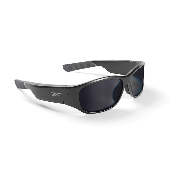 The Reebok Nitrous Smart Audio Sunglasses feature a black wraparound design, dark polarized lenses, and a side Reebok logo, displayed on a white background.