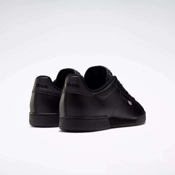 Two black leather Reebok Men's NPC II Shoes are displayed on a white background—one facing forward, the other turned to show the side and heel, featuring Reebok logos and a timeless retro court style for men's fashion.