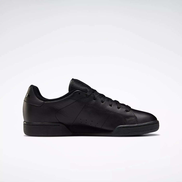 The Reebok Men's NPC II Shoes are black low-top sneakers with a smooth leather upper, black laces, and a subtle heel logo, featuring retro court style. Displayed in profile on a plain light gray background.