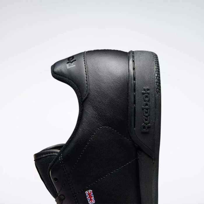Close-up of a black leather Reebok Men's NPC II Shoe with a retro court design, shown sideways to highlight the Reebok logo on the side and tongue against a plain light background.