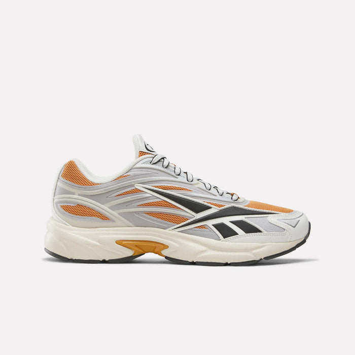An apricot, chalk, and silver athletic shoe with black accents is displayed in a side view on a plain white background. The Reebok Premier Road 1000 Shoes evoke classic Y2K sneakers, featuring mesh and synthetic overlays with a thick white EVA midsole and black tread for enhanced comfort and style.