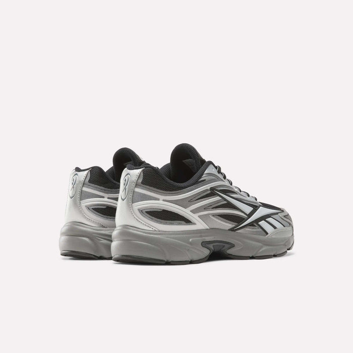 A pair of Reebok Premier Road 1000 Shoes in silver and black are displayed on a white background, showcasing the side and back details with visible mesh panels and reflective accents. Inspired by Y2K sneakers, these retro running shoes combine nostalgic style with modern performance elements.