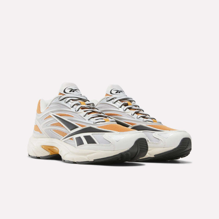 The Reebok Premier Road 1000 Shoes are a pair of athletic sneakers inspired by Y2K designs, showcasing white, orange, gray, and black accents. Crafted from mesh and synthetic materials with lace-up fronts, they feature an EVA midsole for enhanced comfort and chunky rubber soles. The shoes are positioned side by side on a plain white background.