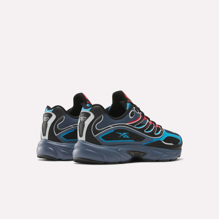 The Reebok Premier Road Control Shoes in black, blue, and gray with red accents feature a chunky sole and mesh details, showcased against a plain white background.