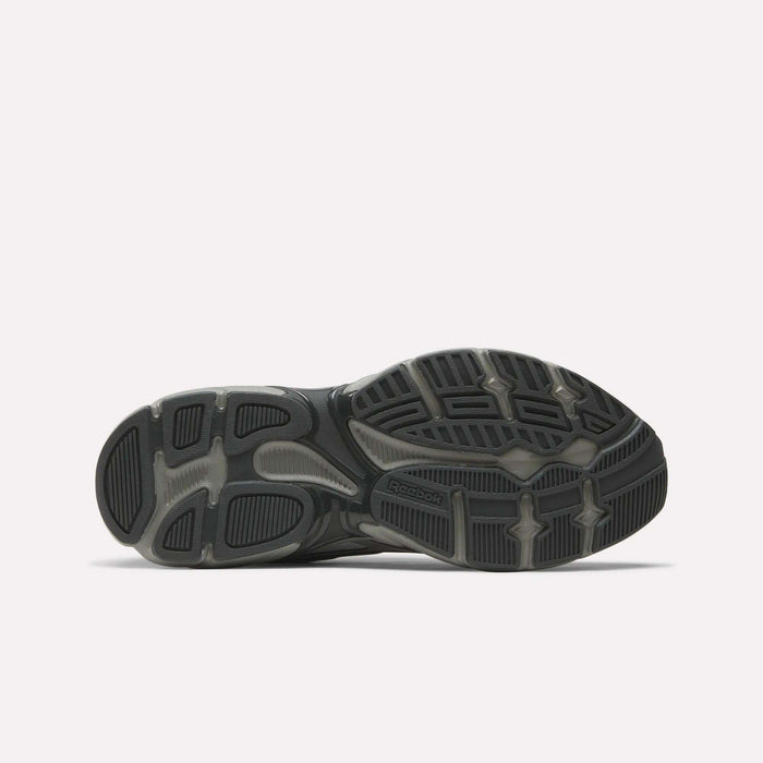 The image shows the sole of Reebok Premier Road Control Shoes, mainly black and gray, with textured rubber patterns and grooves for traction. The Reebok logo appears near the center, reflecting these classic retro running shoes.