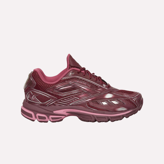 The Reebok Premier Road Ultra Shoes feature a maroon mesh upper with pink accents, silver detailing, and laces. A thick textured sole offers comfort and stability, making them ideal for running or casual wear.