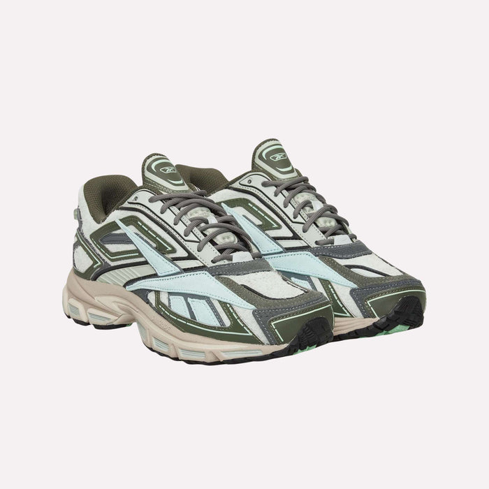 A pair of Reebok Premier Road Ultra Shoes featuring layered paneling in green, gray, and white hues sit side by side on a white background; their design showcases an archival running silhouette with lace-up fronts and thick soles equipped with a dual-density midsole.