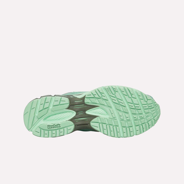 The image displays the sole of a Premier Road Ultra Shoe by Reebok in light green, highlighting its textured tread patterns and the Reebok logo near the heel. This archival running silhouette features a dual-density midsole, offering enhanced comfort and support. The background is plain white.
