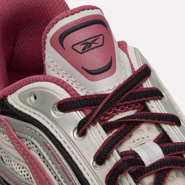Close-up of the Reebok Premier Road Ultra Shoes in pink, white, and gray, highlighting the laces, breathable mesh upper, and Reebok logo on the tongue. The partially visible dual-density midsole suggests enhanced comfort and support.