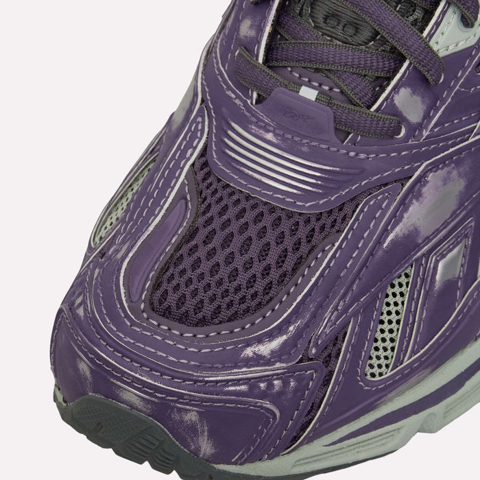 Close-up of the front of a purple Reebok Premier Road Ultra Shoes sneaker, featuring a shiny, textured upper with mesh fabric, white scuff marks, and gray accents along the sole and stitching. This classic archival running silhouette by Reebok is upgraded with a dual-density midsole for enhanced comfort and support.