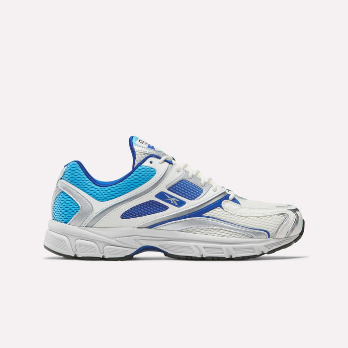 The Reebok Premier Trinity Shoes are white athletic sneakers with blue and silver accents, mesh panels, and a thick gray sole, shown from the side on a plain light background for a retro tech look.