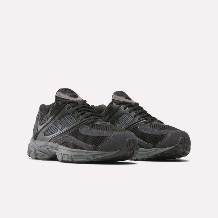 A pair of Reebok Premier Trinity Shoes for women in black, featuring mesh and synthetic overlays, thick rubber soles, and lace-up closures, shown on a plain white background for a retro running vibe.