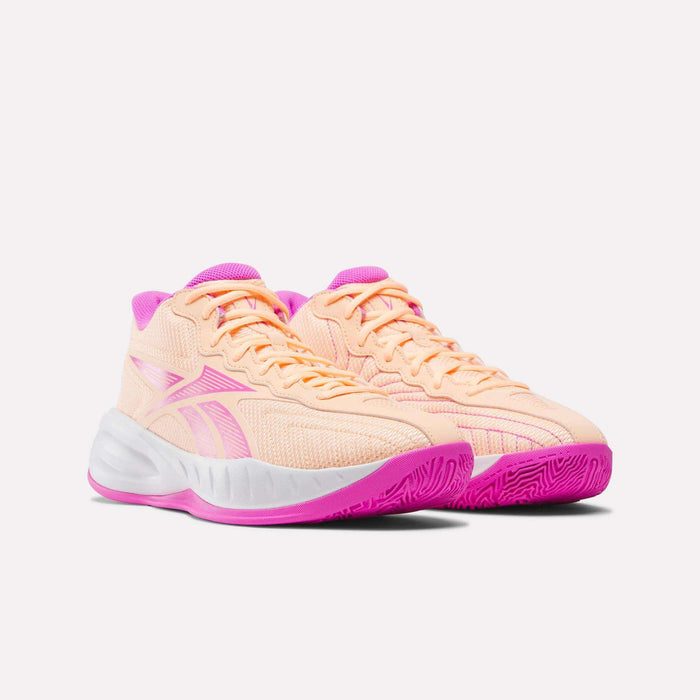 A pair of peach Press Basketball Shoes by Reebok with bright pink accents on the tongue, sole, and logo, featuring EVA cushioning for soft, responsive comfort—all shown against a plain white background.