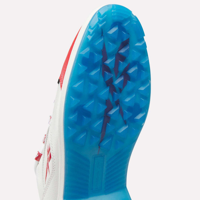 Close-up of the bottom of a white Reebok Question Golf Shoe with red accents, featuring a bright blue spikeless sole and prominent triangular traction patterns.