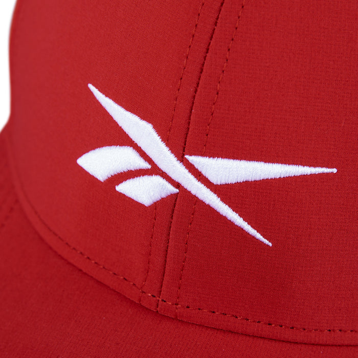 Close-up of the Reebok Range Cap, a red golf hat with a white embroidered logo of angled lines and shapes on the front panel, offering sun protection and moisture-wicking comfort.