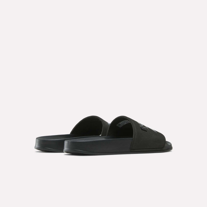 The Reebok RBK Fulgere Swim Slides are shown in black from a rear-side angle, highlighting their open-toe slip-on design and thick sole against a plain white background.