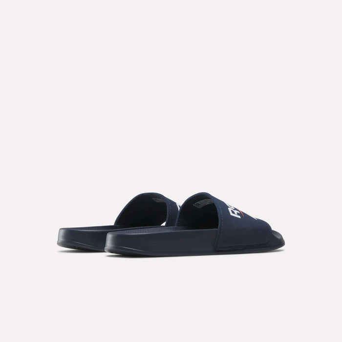 A pair of Reebok RBK Fulgere Swim Slides in navy blue are placed side by side on a plain white background, with the left slide turned outward and the right featuring part of a white Reebok logo on its upper strap.