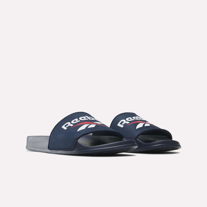 A pair of Reebok RBK Fulgere Swim Slides in navy blue with white and red branding on the straps, shown from a low front angle against a plain white background.