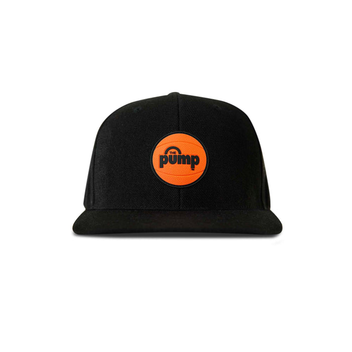 The Reebok Pump Hat by Reebok is a black snapback with a flat brim, featuring an orange basketball-like patch on the front labeled "pump" in black letters.