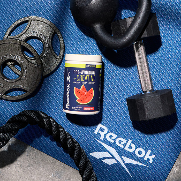 A blue Reebok exercise mat holds a dumbbell, weight plates, battle rope, and a container of Reebok ReeEnergize Pre-Workout + Creatine with a watermelon label—perfect for boosting your workout endurance.