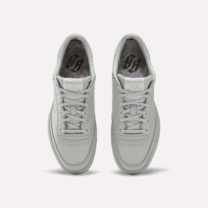 A pair of Reebok x BBC Club C 85 Shoes in white are displayed side by side on a light background, viewed from above to showcase their laces, perforated toe boxes, and grey insoles featuring a black printed Reebok logo. Expertly crafted from premium materials, these heritage sneakers highlight the collaboration between Reebok and BBC.