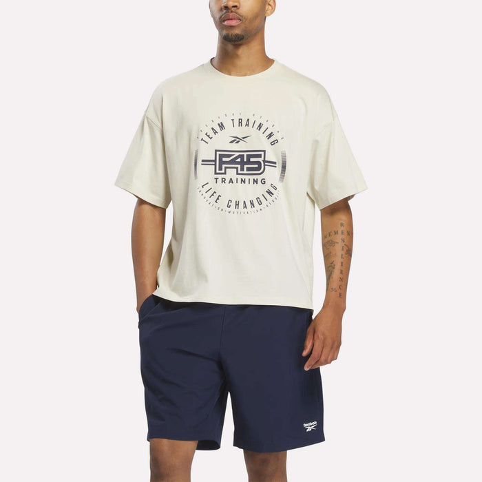 A man wearing a linen Reebok X F45 Training Graphic T-Shirt stands against a plain white background, showcasing a stylish men's fitness shirt by Reebok that's perfect for workouts and casual wear.