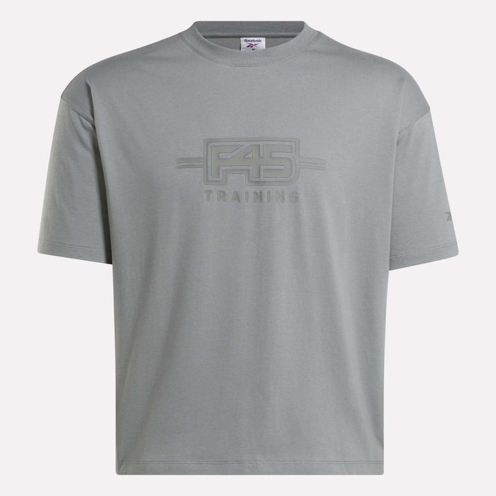 The Reebok x F45 Training Graphic T-Shirt is a gray oversized tee featuring the F45 TRAINING text and a stylized F45 logo on the chest. With short sleeves and a crew neckline, this classic Reebok shirt offers unmatched comfort—perfect for representing your passion during any Reebok x F45 Training session.