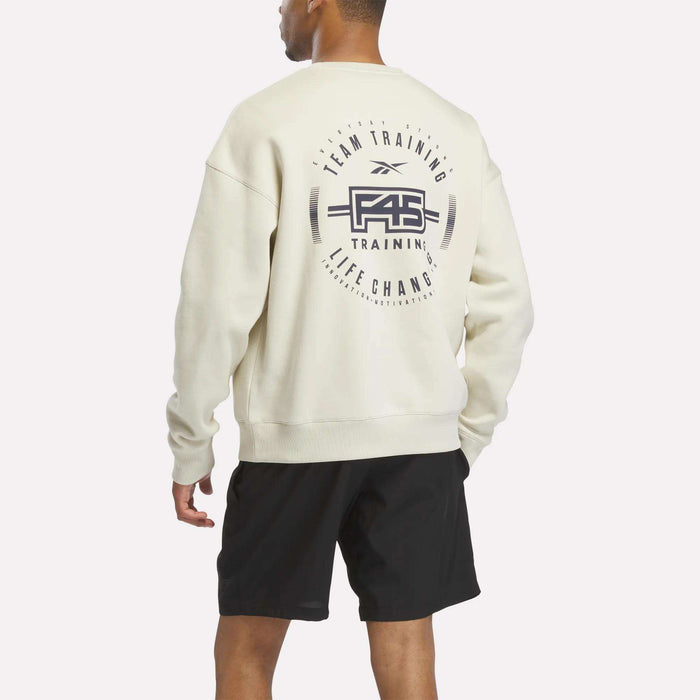 A man wearing a cream Reebok x F45 Training Relaxed Graphic Sweatshirt with a barbell and F45 Training design on the back, paired with black shorts, stands facing away.