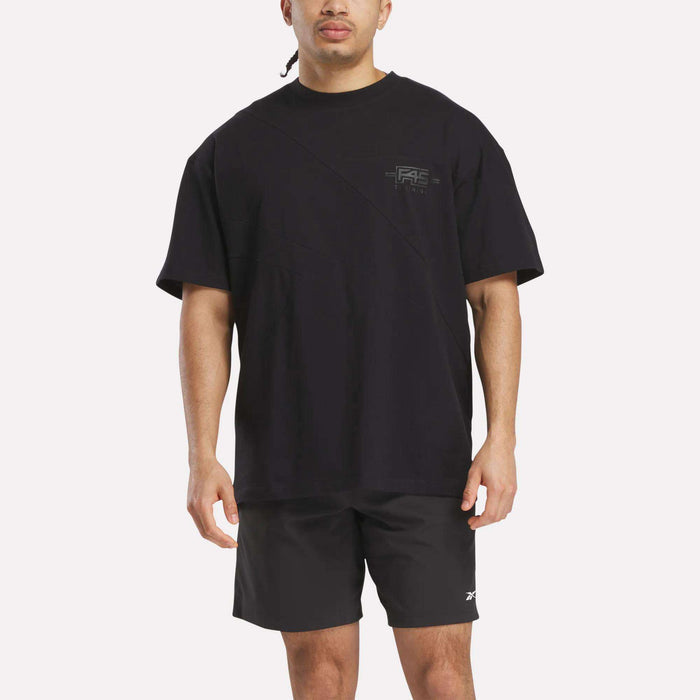 A man wears a Reebok x F45 Training Relaxed T-Shirt and black shorts, standing facing forward against a plain white background.