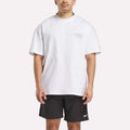 A man stands facing forward in a loose Reebok x F45 Training Relaxed T-Shirt, featuring a small logo on the left chest and black Reebok performance shorts, set against a plain light background.