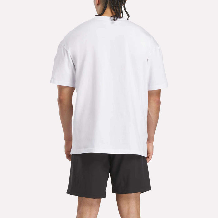 A person is standing and facing away from the camera, wearing a plain white Reebok x F45 Training Relaxed T-Shirt and black shorts against a light background.