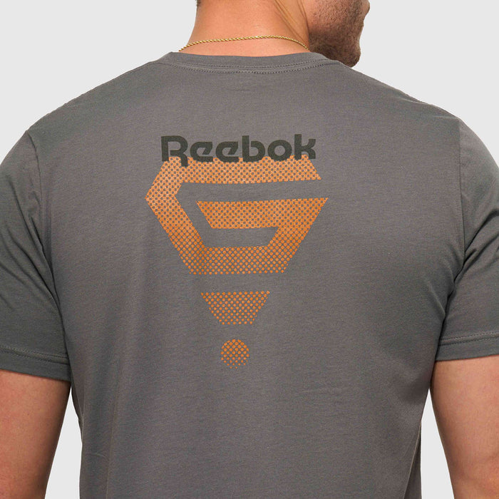 A person faces away from the camera, wearing the Reebok x GLDN PNT Jersey Tee—a gray premium cotton shirt with a large orange Reebok logo and geometric design on the back, styled by Reebok for everyday comfort.
