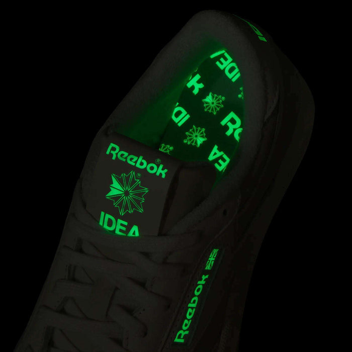 A close-up of the Reebok x IDEA Club C 85 Shoes in black highlights glowing bright green Reebok logos and the word “IDEA”—inspired by the creative vibe of IDEA bookstore—on both the tongue and inner sole.