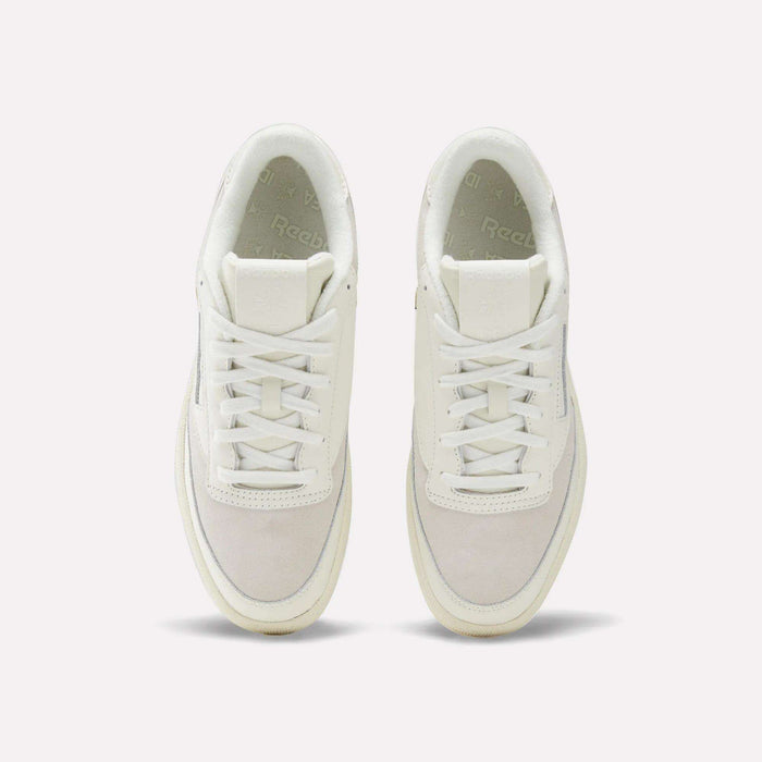 Top-down view of a pair of Reebok x IDEA Club C 85 Shoes, featuring cream-colored laces, suede toe boxes, and signature Reebok branding on the tongue and insole. Set against a plain, light grey background, this design blends effortlessly with the nostalgic vibe you’d expect to find among vintage books at the IDEA bookstore.