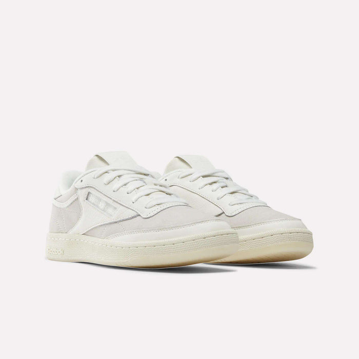 The Reebok x IDEA Club C 85 Shoes by Reebok are white low-top sneakers featuring beige soles, white laces, and subtle logo detailing on the side, showcased against a plain white background.