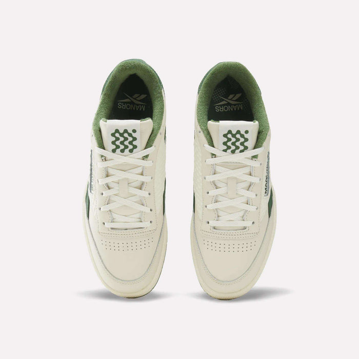 Top view of a pair of Reebok x Manors Club C Revenge Golf Shoes in cream and green with white laces. The tongue and inner lining are green, featuring wavy green lines and the word “MANNORS,” reminiscent of the premium collaboration between Reebok and Manors golf shoes. The shoes have perforated toe boxes.