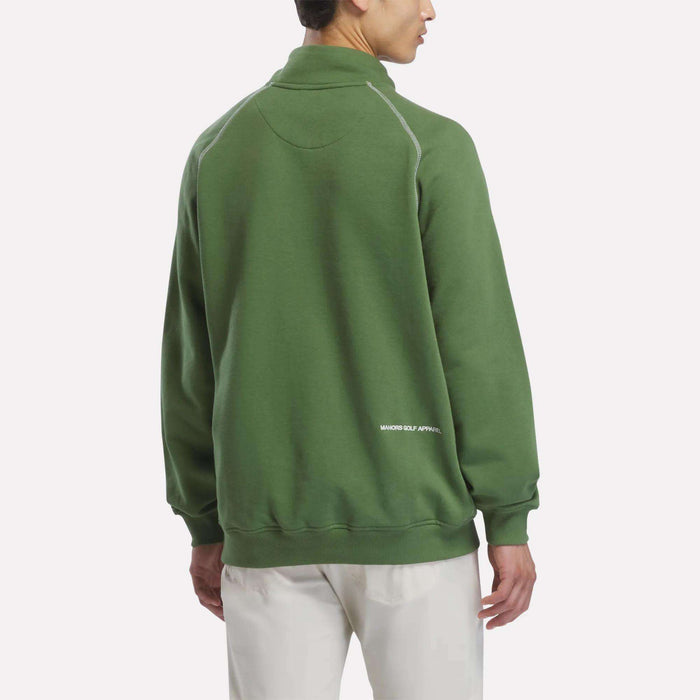 A person wearing a green Reebok x Manors Men’s Quarter-Zip Pullover and white pants stands facing away, displaying the back of the sweatshirt with “MAJOR GOLF APPAREL” text near the hem, from the Reebok collection.