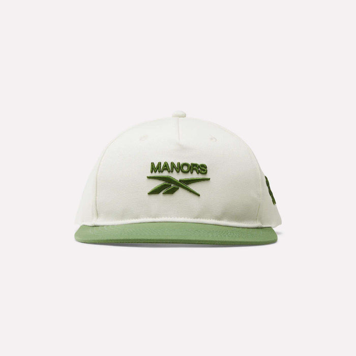 The Reebok x Manors Men’s Retro Crown Cap features a crisp white design with a green brim and green embroidered MANORS text and logo on the front. This classic golf cap from Reebok includes an adjustable snapback for a perfect fit and is shown against a simple light background.