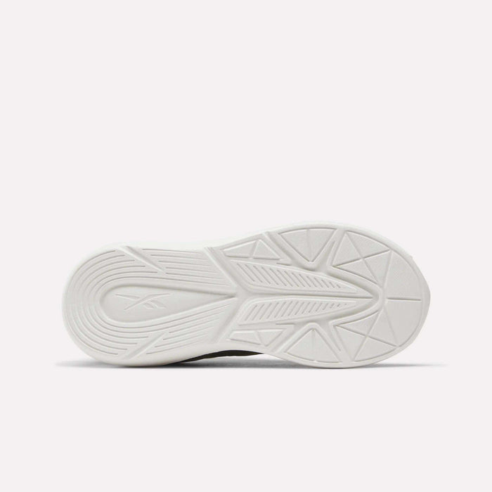 A white rubber sole featuring geometric tread patterns with lines and triangles is shown against a plain white background. Designed as running shoes for kids, the Reebok Rush Runner 6.0 Elastic Lace Top Strap Running Shoes showcase the Reebok logo embossed near the heel for both style and all-day comfort.