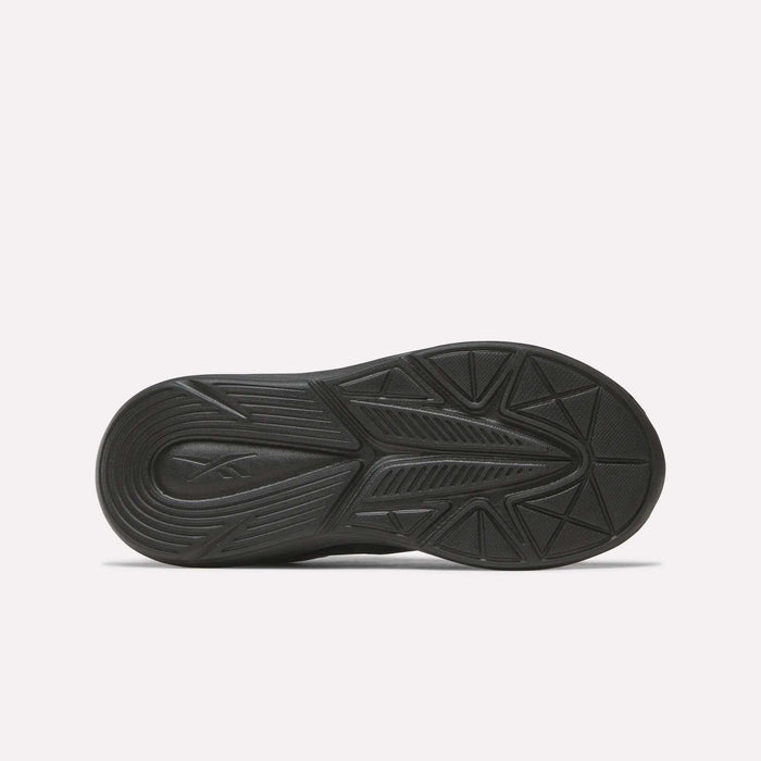 The image shows the black rubber outsole of Reebok Rush Runner 6.0 Elastic Lace Top Strap Running Shoes for little kids, featuring geometric tread patterns for traction and comfort, viewed from below against a plain white background.