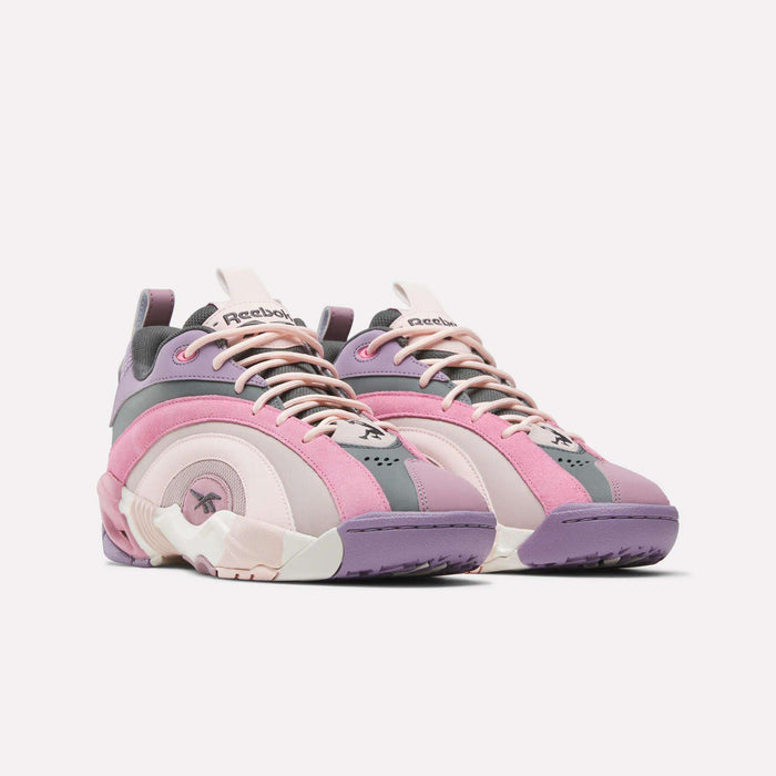 The Reebok Shaqnosis Low Shoes, shown against a plain white background, feature wavy design lines and Hexalite cushioning in shades of pink, purple, and gray with cream accents.