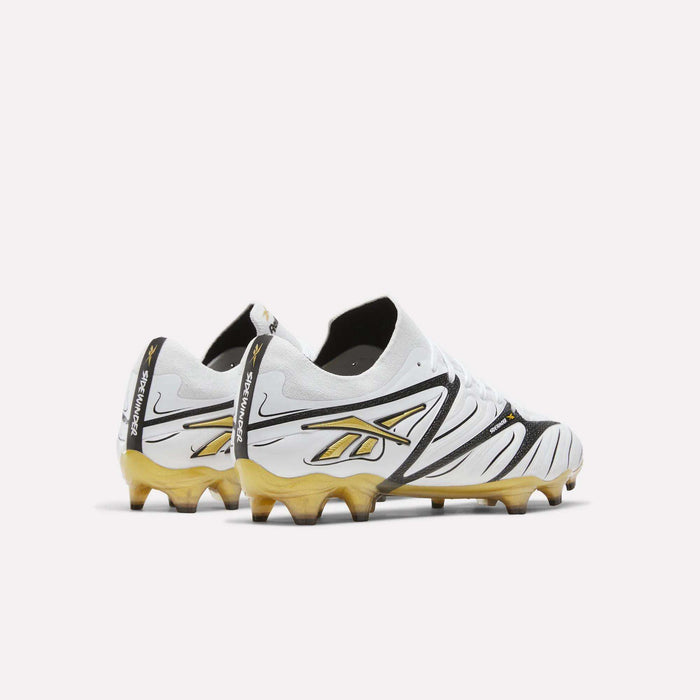 The Reebok Sidewinder 26 Elite Firm Ground Cleats feature a stylish white and gold colorway with black accents, showcased from the back and side to highlight the signature Reebok logo and distinctive wavy design on the heel and sides. Designed for superior ball control on firm grass surfaces, these cleats blend performance with standout style.