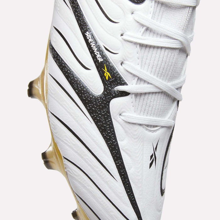 Close-up of the Reebok Sidewinder 26 Elite Firm Ground Cleats in white, featuring black and gold accents, textured detailing for improved ball control, and Reebok branding near the laces—ideal for play on firm grass surfaces.