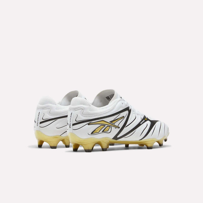 A pair of Reebok Sidewinder 26 Pro Firm Ground Cleats in white, featuring black and gold accents, including a gold Reebok logo and gradient gold soles, designed to enhance ball control, displayed against a plain white background.