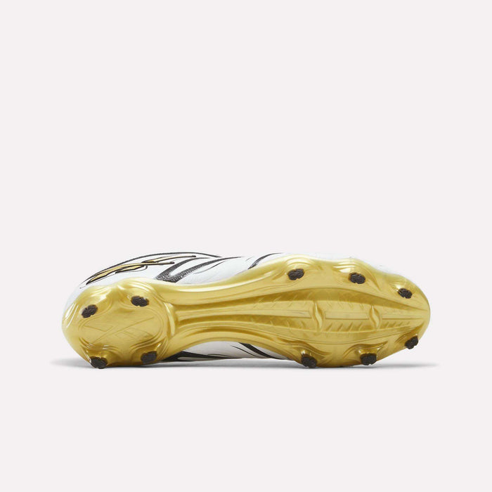 A pair of Reebok Sidewinder 26 Pro Firm Ground Cleats in white and black is displayed with the gold-colored sole facing up, revealing multiple studs for firm ground traction. Designed for enhanced ball control, these soccer cleats are positioned against a plain, light-colored background.