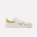 The Reebok Smash Edge Shoes feature a white design with beige and gold accents and the Reebok logo on the side and heel—ideal for fans of classic indoor soccer style, shown against a plain white background.