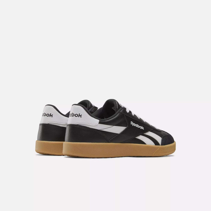 The Reebok Smash Edge Shoes feature a minimalist black-and-white design with gum-colored soles, inspired by classic court style, shown from the back and side on a plain white background.