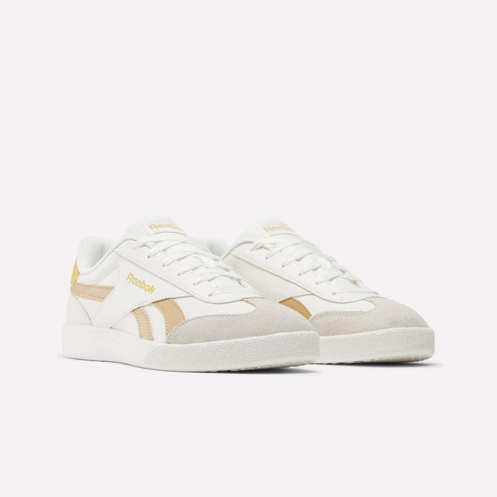 The Reebok Smash Edge Shoes feature white uppers, beige suede toe caps and side stripes, yellow accents, and white laces—an ideal choice for stylish indoor soccer.